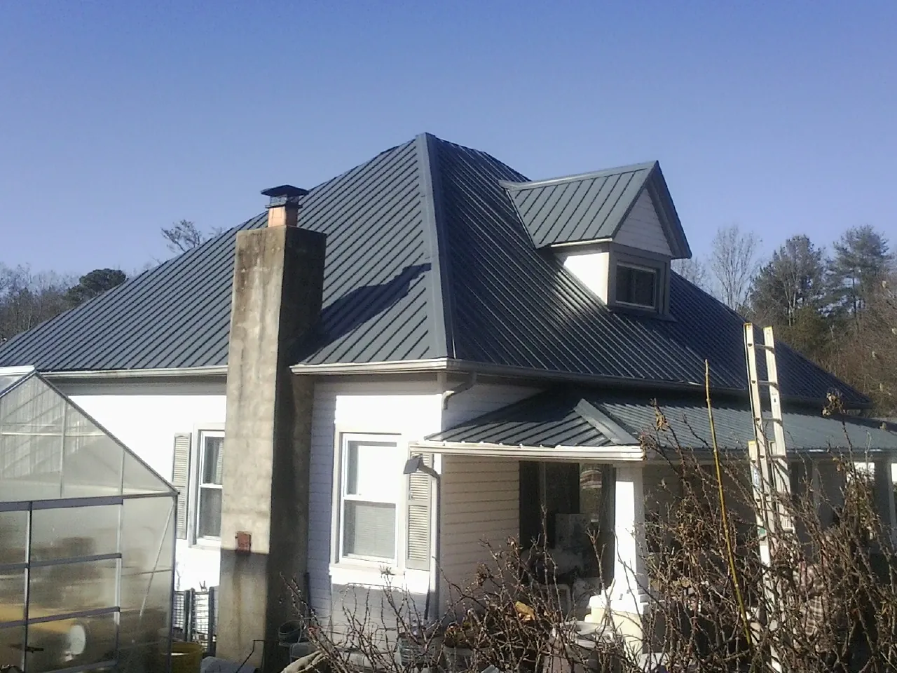 Dark blue standing seam metal roof on a white farmhouse with dormer — Slate & Tile Roof Repair by Roofing Brothers in North Washington