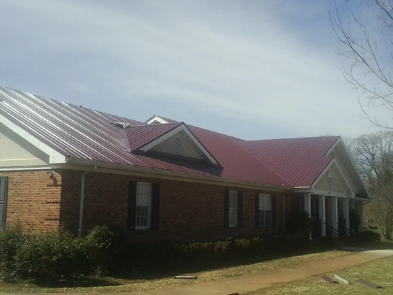 Red metal roof with gabled entries on a long brick building, from a Hail Damage Roof Repair job in North Washington