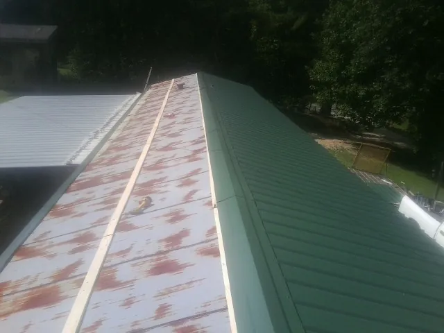 Old rusted panels beside newly installed green metal roofing — Wind Damage Roof Repair by Roofing Brothers in North Washington