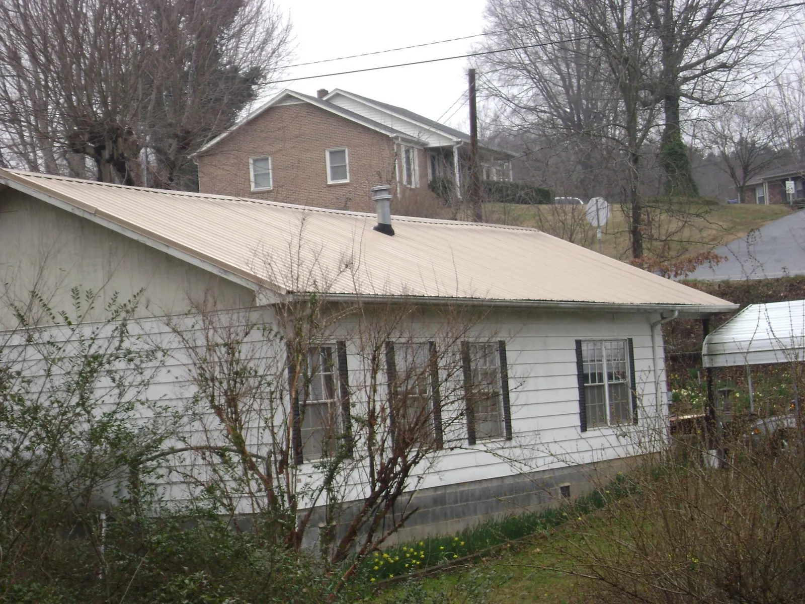 Tan metal roof on a white sided house set into a hillside — Commercial Roofing by Roofing Brothers in North Washington